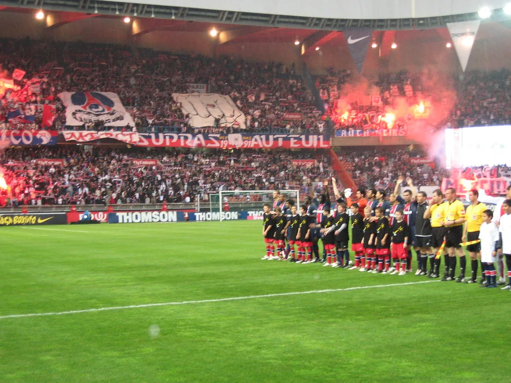 PSG and visiting players line up on the pitch at Parc des Princes as fans light flares behind them