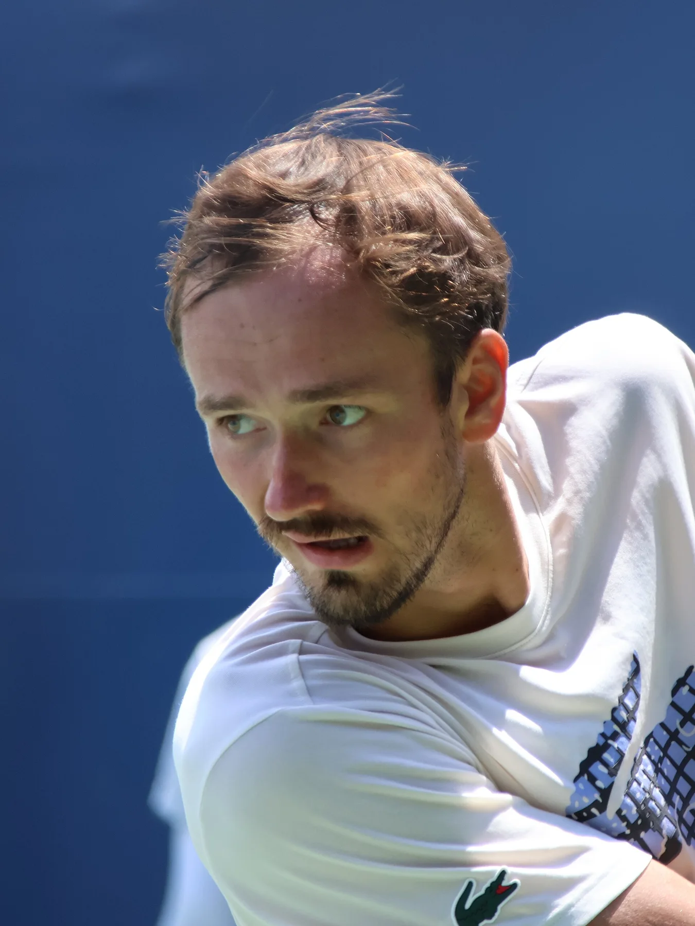 Daniil Medvedev in a white shirt looks over his shoulder during a match against a blue backdrop