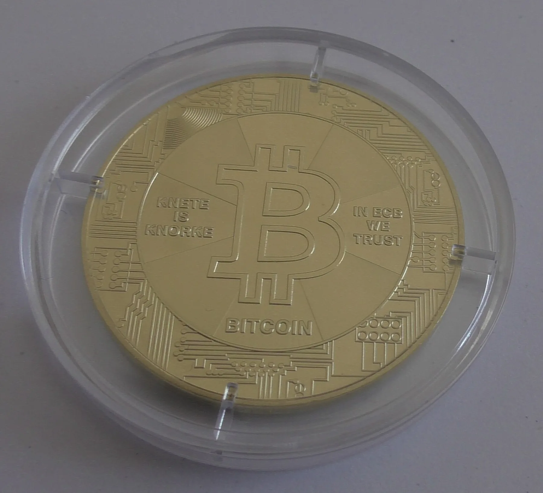 Gold-coloured novelty bitcoin coin with the B logo and circuit pattern in a clear plastic case