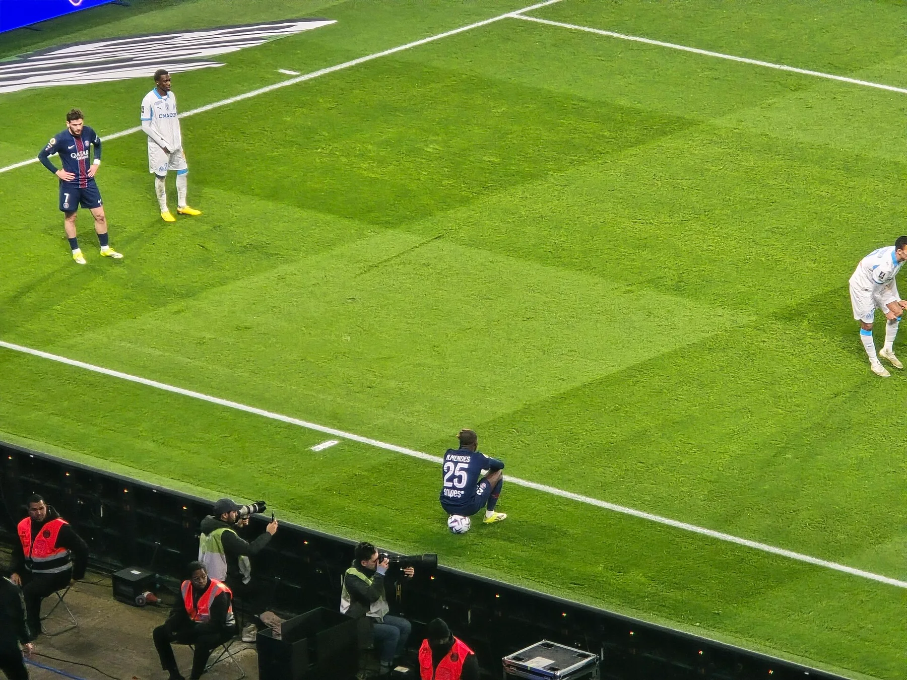 PSG players in dark blue kits on the pitch during a match, photographers along the touchline