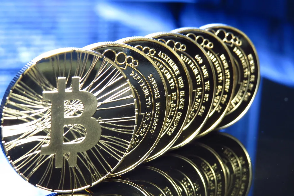 Row of gold-coloured physical bitcoin coins standing on edge against a blue background