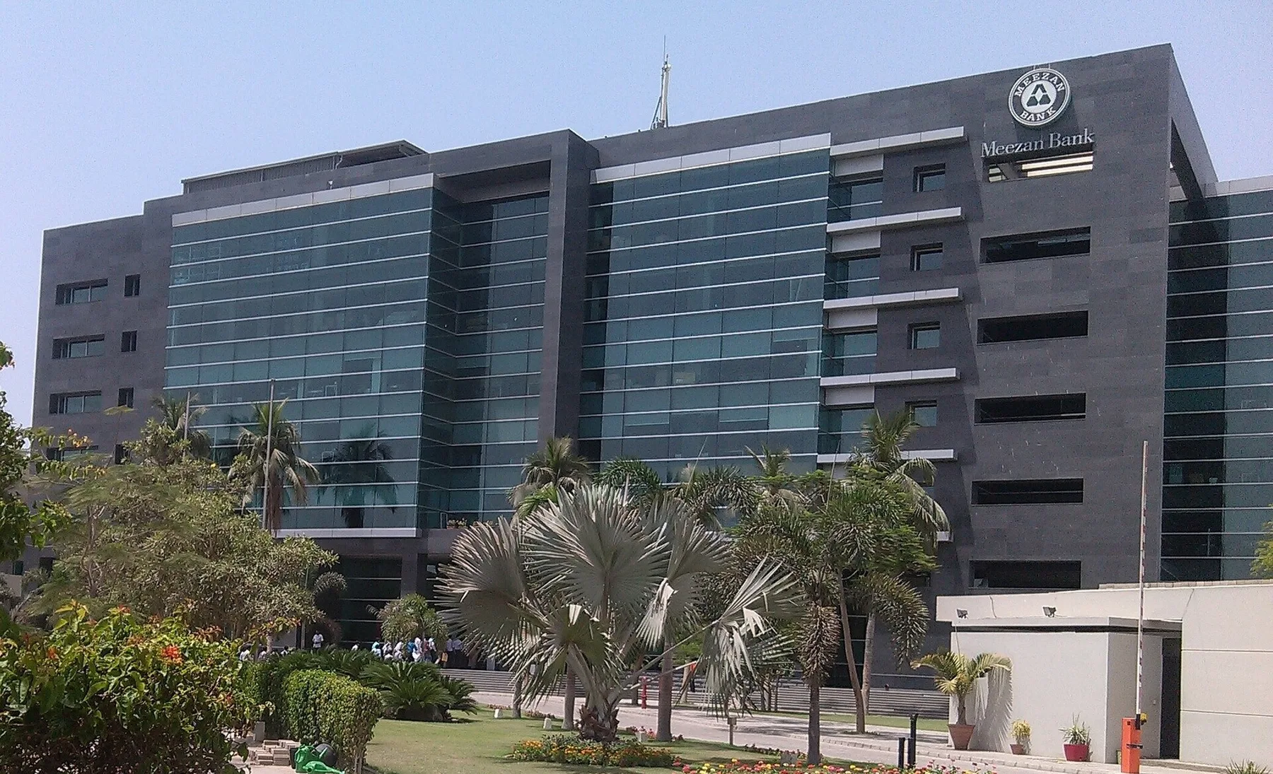 Meezan Bank head office, a dark glass building with the bank logo, behind palm trees and a garden