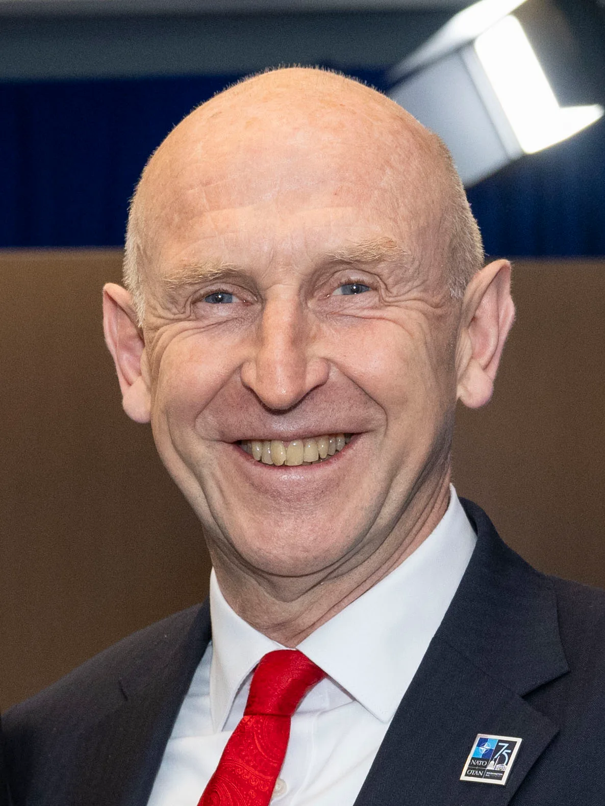 UK Chancellor John Healey smiling in a dark suit, white shirt and red tie with a NATO lapel pin