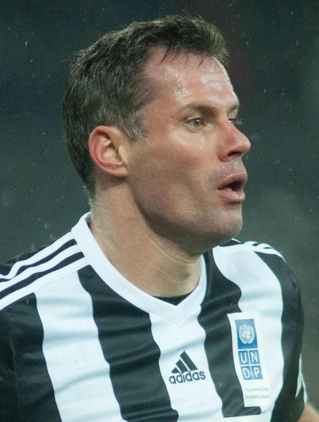 Jamie Carragher in a black and white striped charity match shirt looking to his left