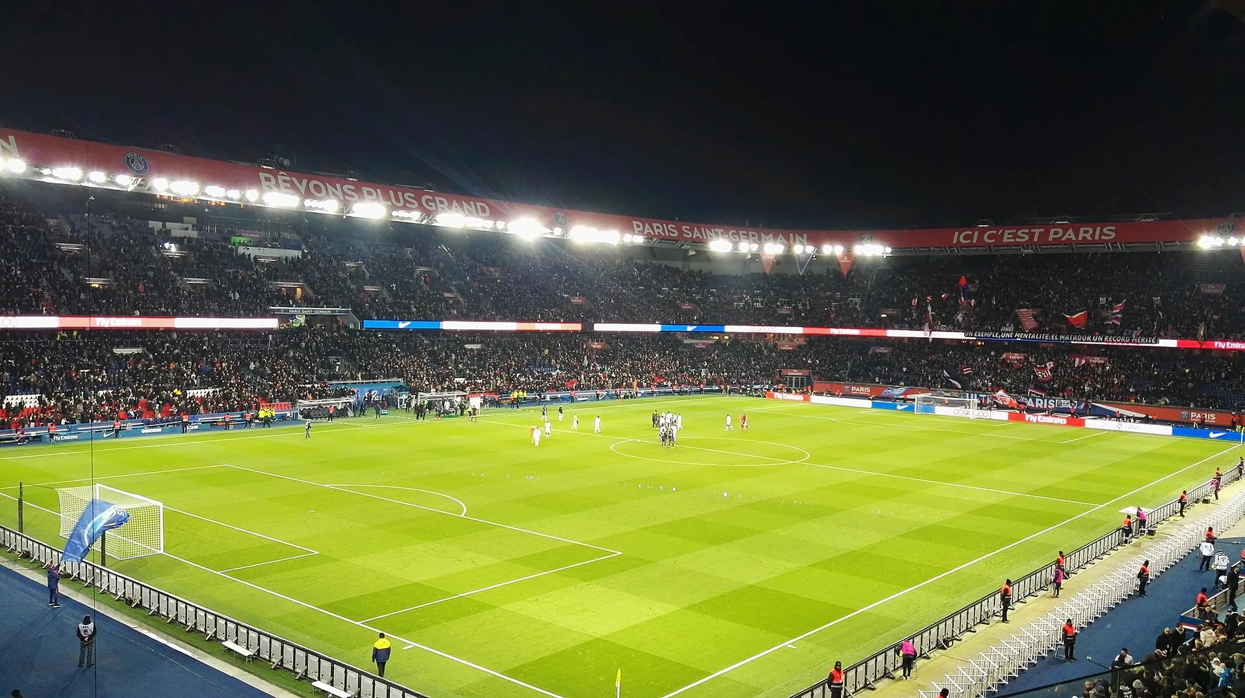 Floodlit Parc des Princes pitch at night, packed stands under red Paris Saint-Germain banners