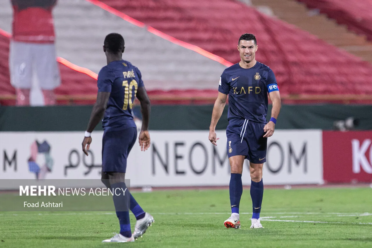 Cristiano Ronaldo in Al Nassr navy kit smiles at a teammate wearing number 10 during an AFC match