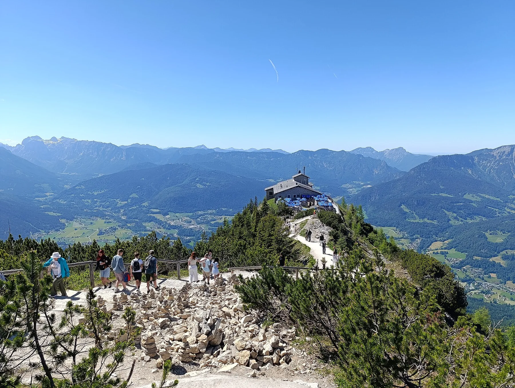 The Kehlsteinhaus on a forested Alpine ridge above Berchtesgaden, with walkers on the path below
