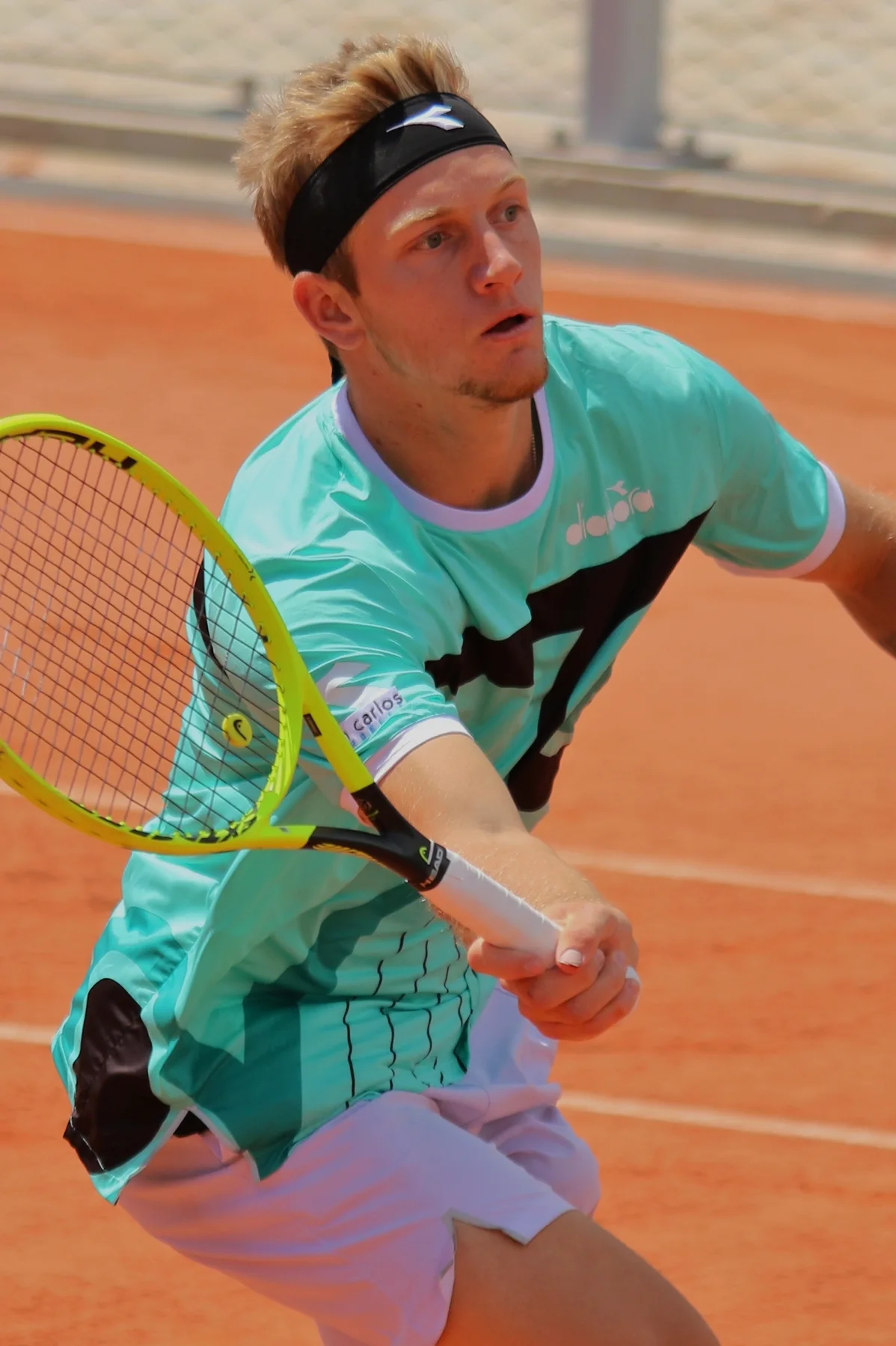 Alejandro Davidovich Fokina in a headband stretches for a forehand on a clay court at Roland Garros