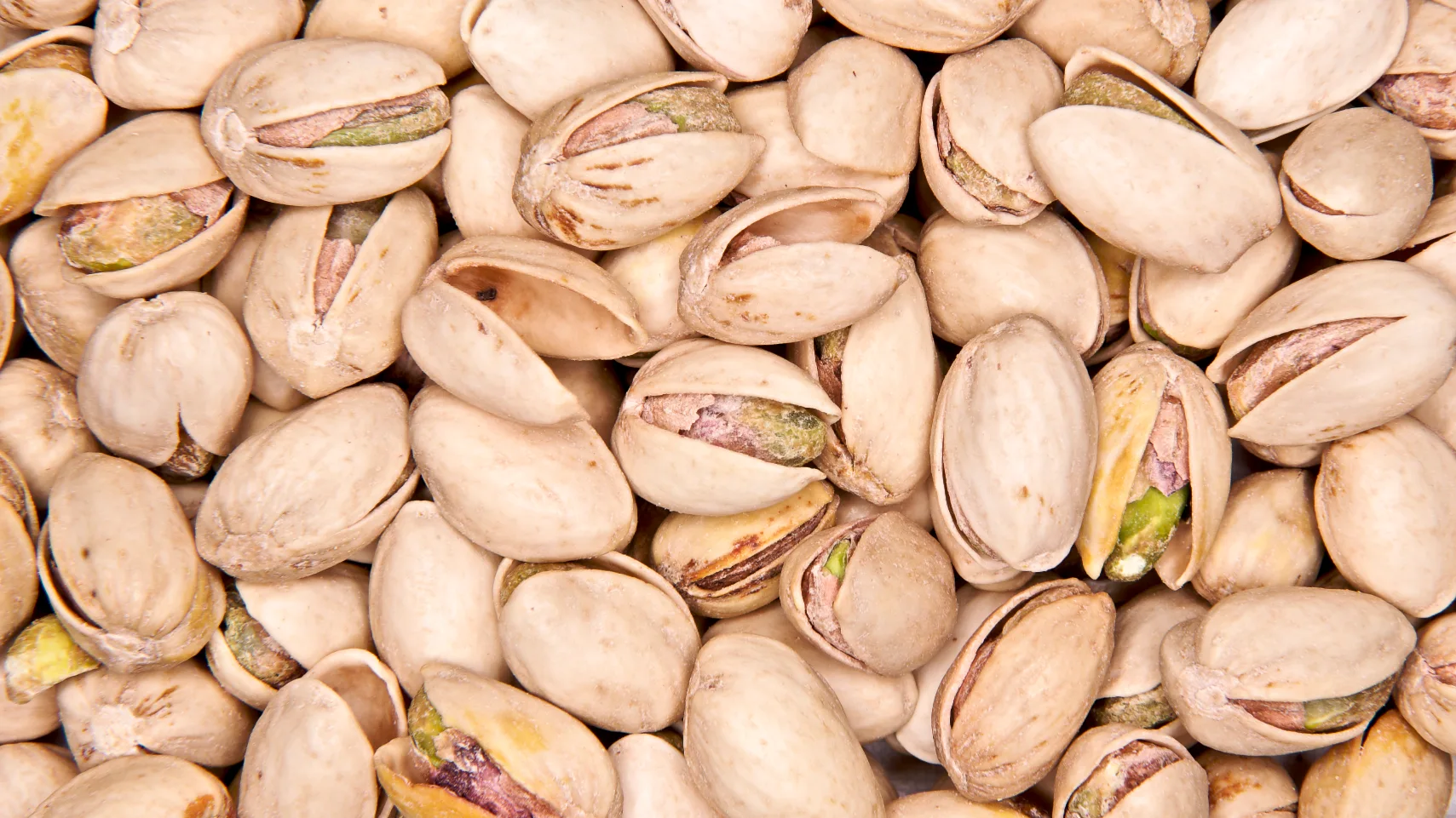 Close-up of a heap of roasted pistachios in their split shells, green kernels showing