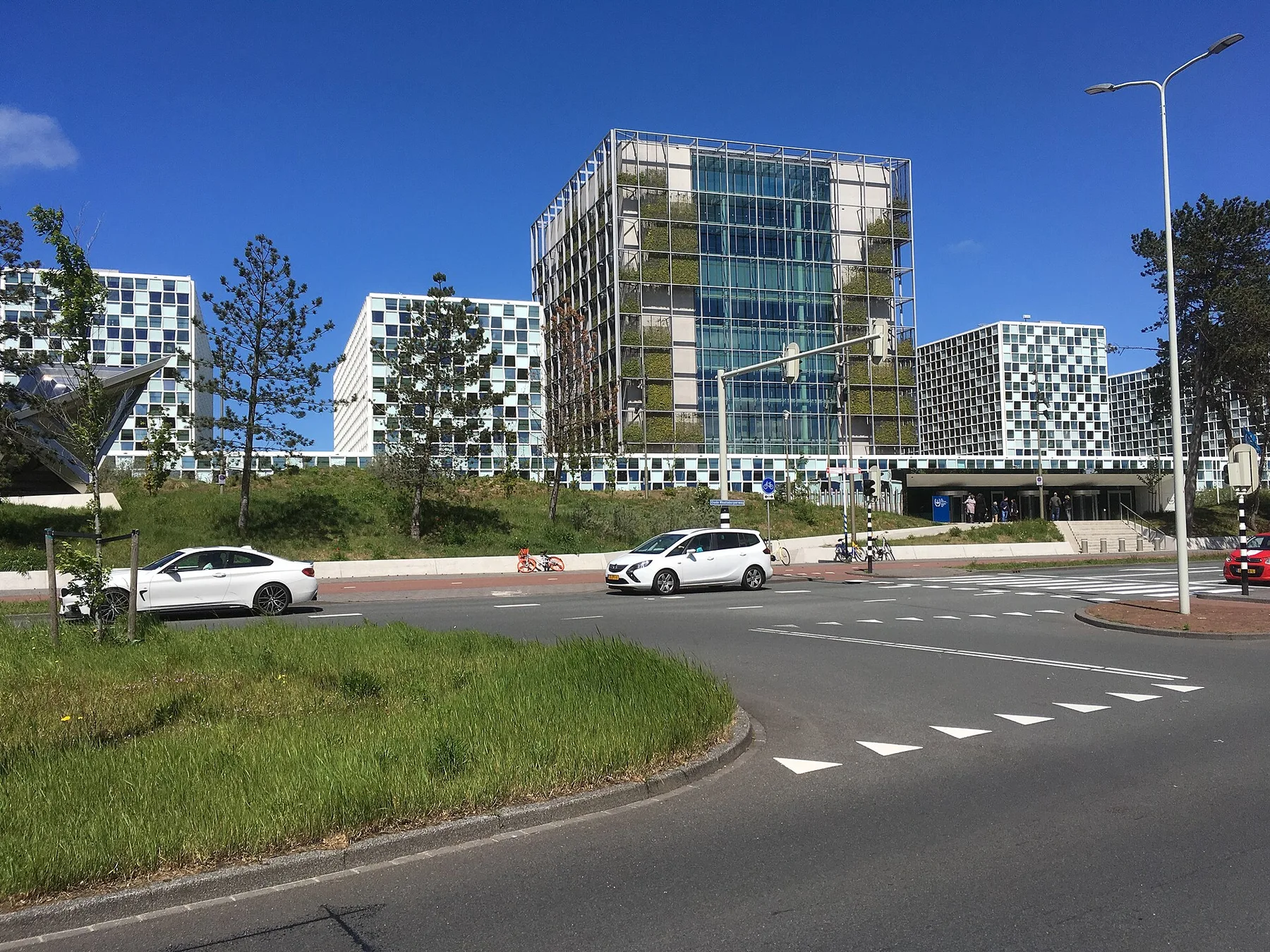 The International Criminal Court building in The Hague, a glass tower with white blocks, seen across a road on a sunny day