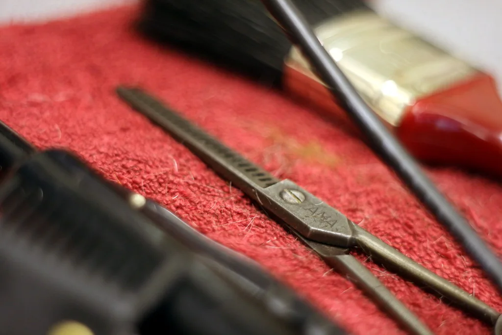 Barber scissors, comb, clippers and a brush laid on a red towel