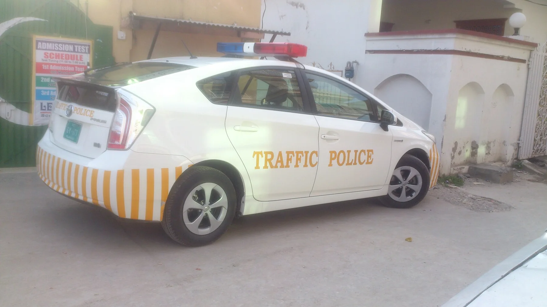 White Toyota Prius traffic police patrol car with roof lights and yellow stripes parked outside a gate