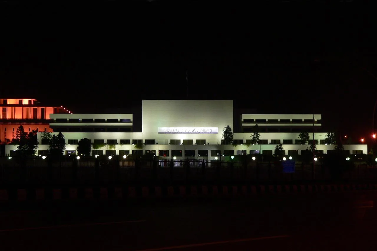 Parliament House in Islamabad lit up at night, its white facade and name sign visible