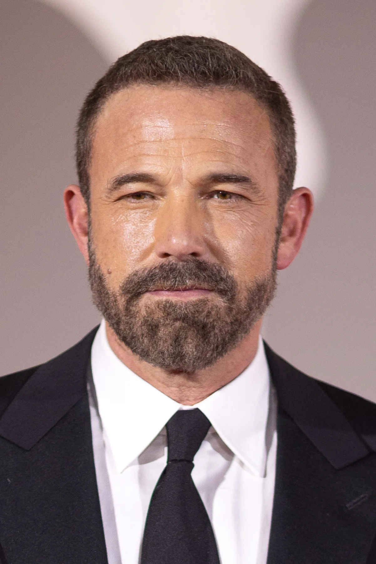 Ben Affleck with a grey beard in a black suit and tie at a film premiere