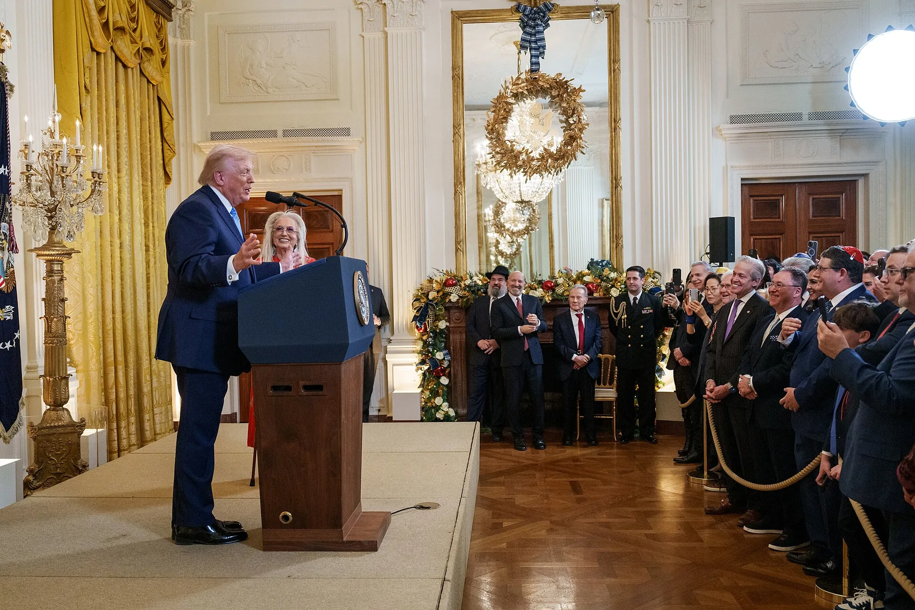 Donald Trump speaks at a podium in the White House East Room as guests watch and applaud