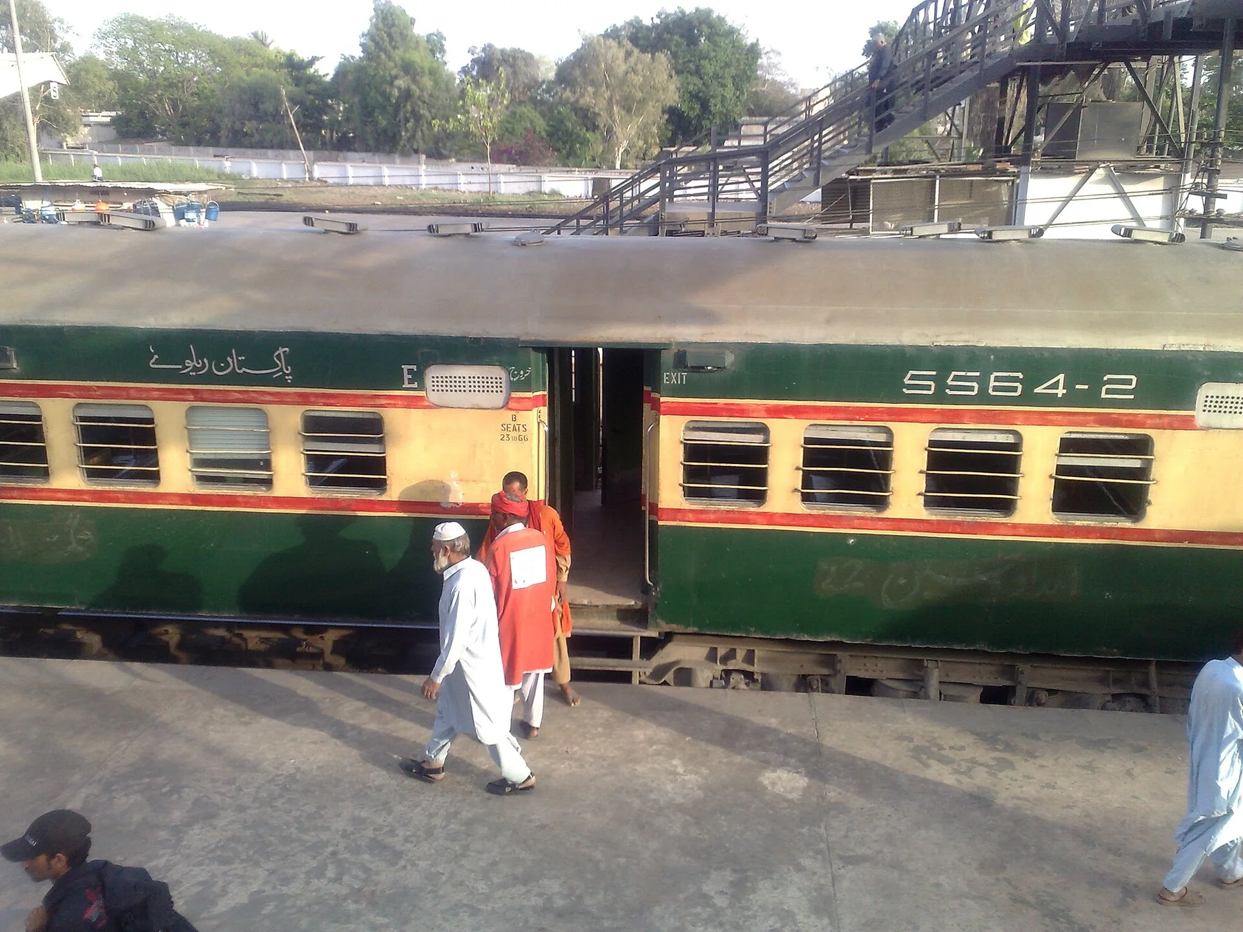 Green and cream Pakistan Railways passenger coach at a station platform, with a porter in a red shirt