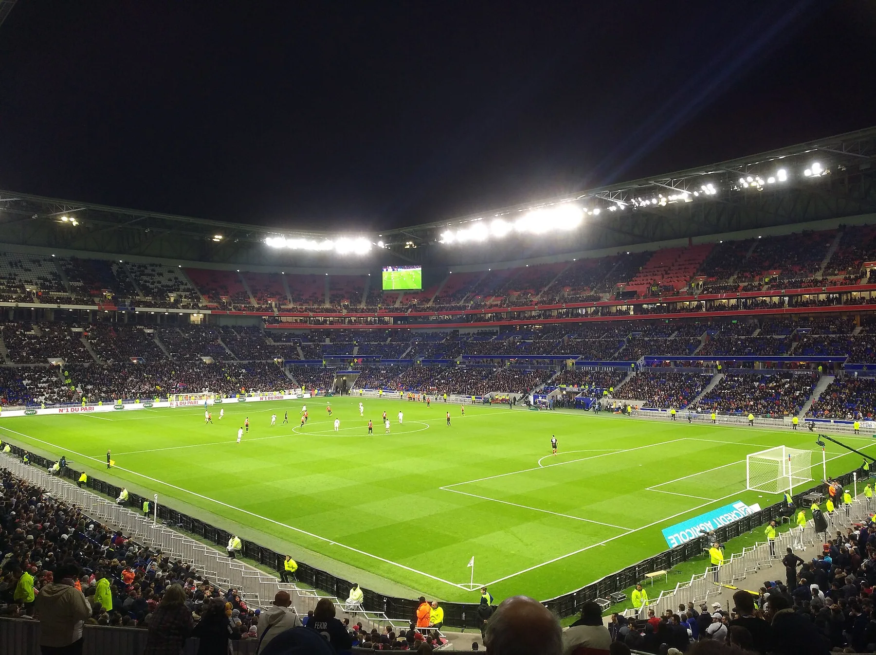 Floodlit Lyon stadium at night with a full crowd watching a match on the green pitch