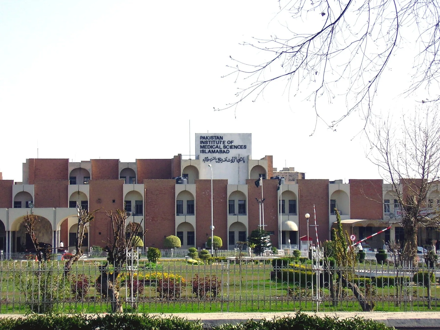 Brick main building of the Pakistan Institute of Medical Sciences in Islamabad with its name sign and front garden