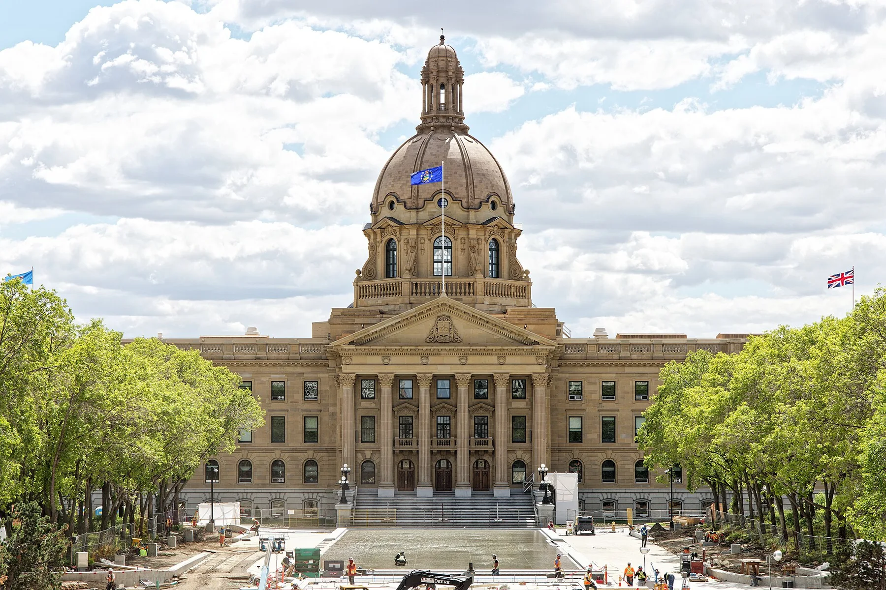 Domed sandstone Alberta Legislature Building in Edmonton with the Alberta flag flying, workers on the plaza in front