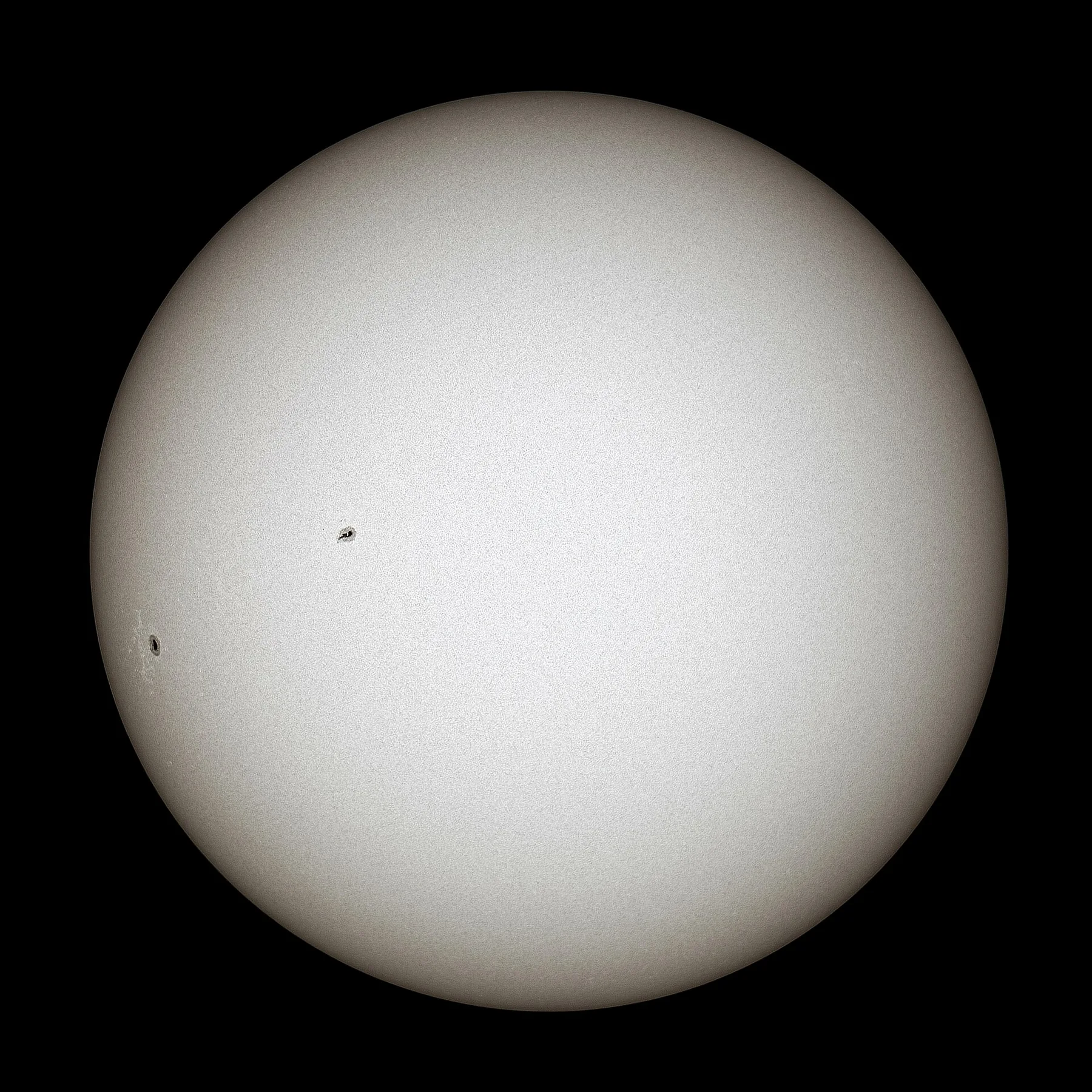 The Sun photographed in white light as a pale disc with two small dark sunspots against black space