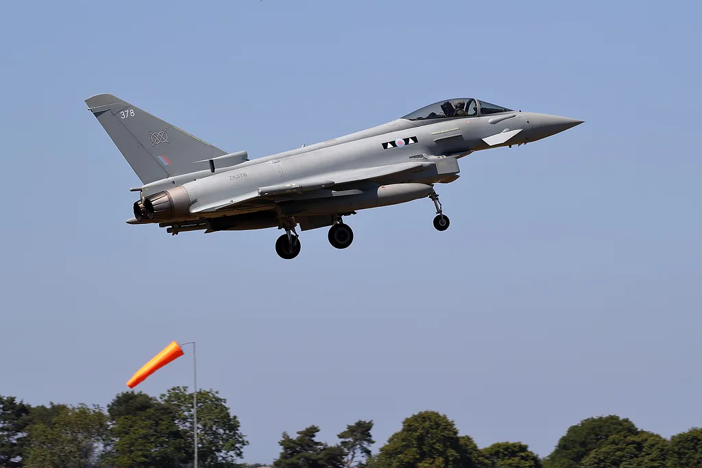 Grey RAF Typhoon fighter jet taking off with landing gear down, an orange windsock below