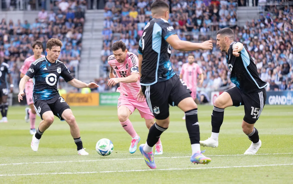 Lionel Messi in Inter Miami pink dribbles the ball past three defenders in dark blue kits during an MLS match