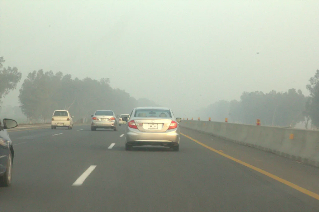 Cars driving in hazy, smoggy conditions on a three-lane stretch of the Lahore-Islamabad M-2 motorway