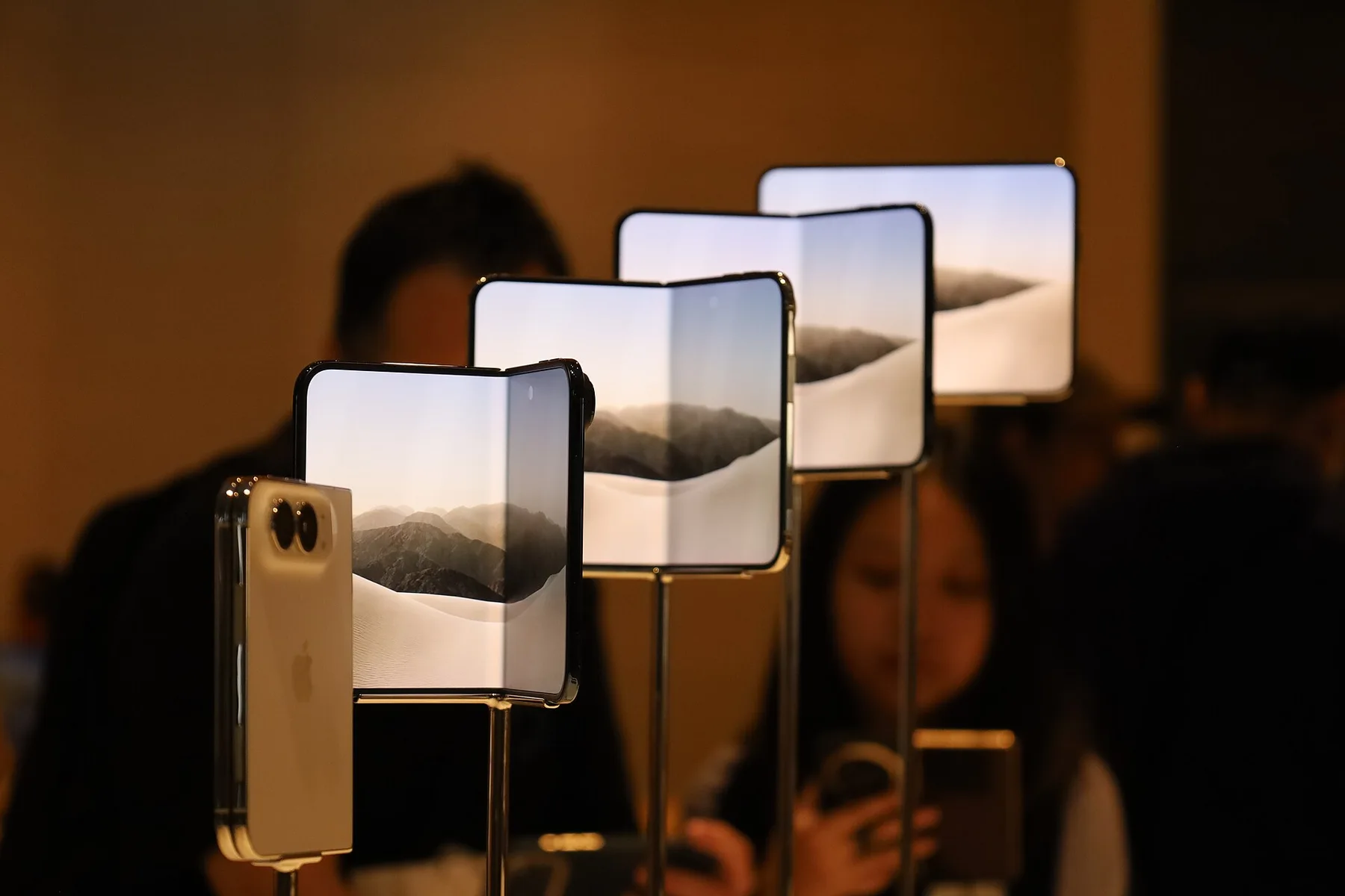 Unfolded iPhone Duo phones on display stands in a row, with a customer looking on behind