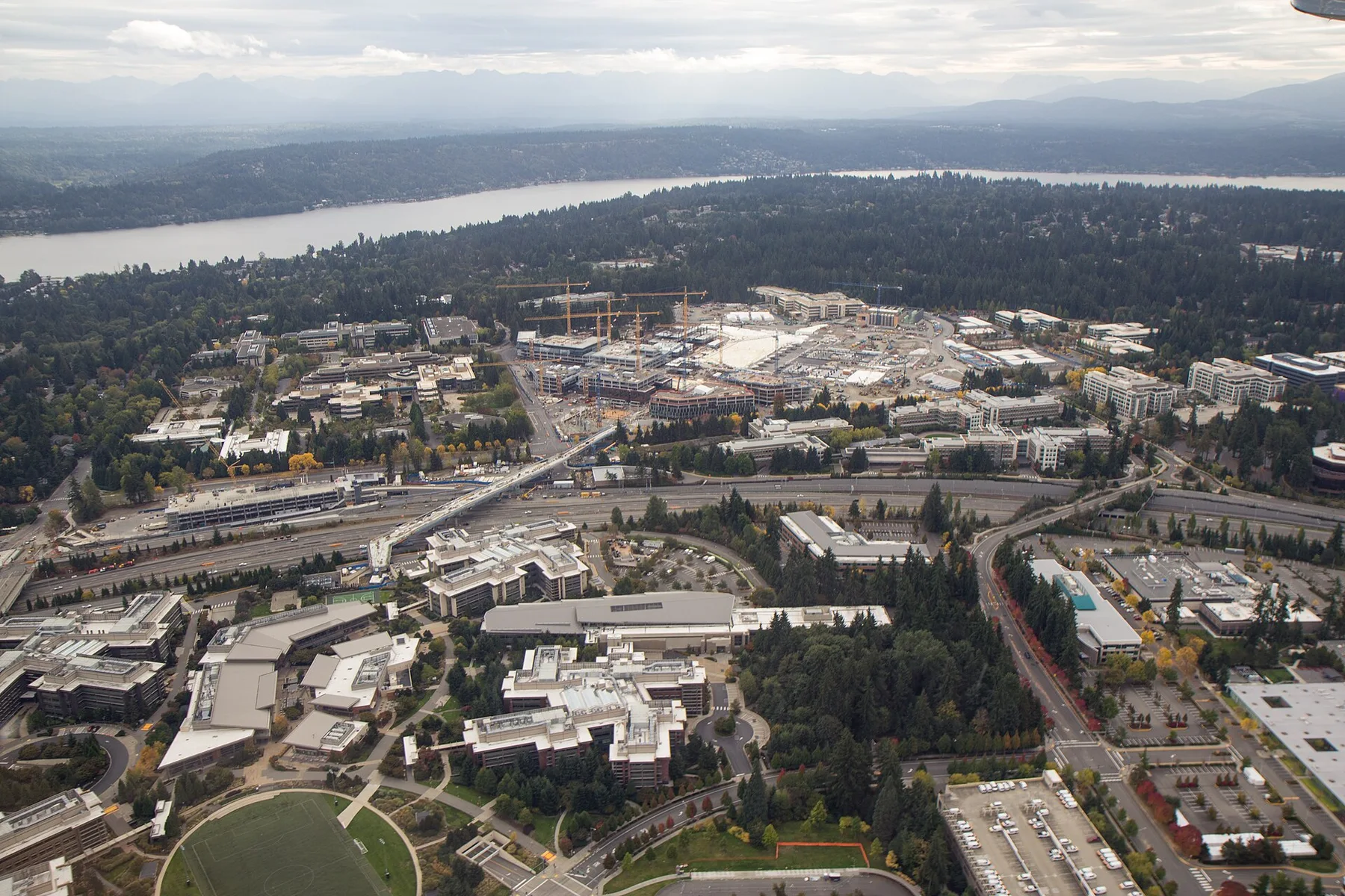 Aerial view of Microsoft's Redmond campus office buildings with construction cranes, a lake and forest behind
