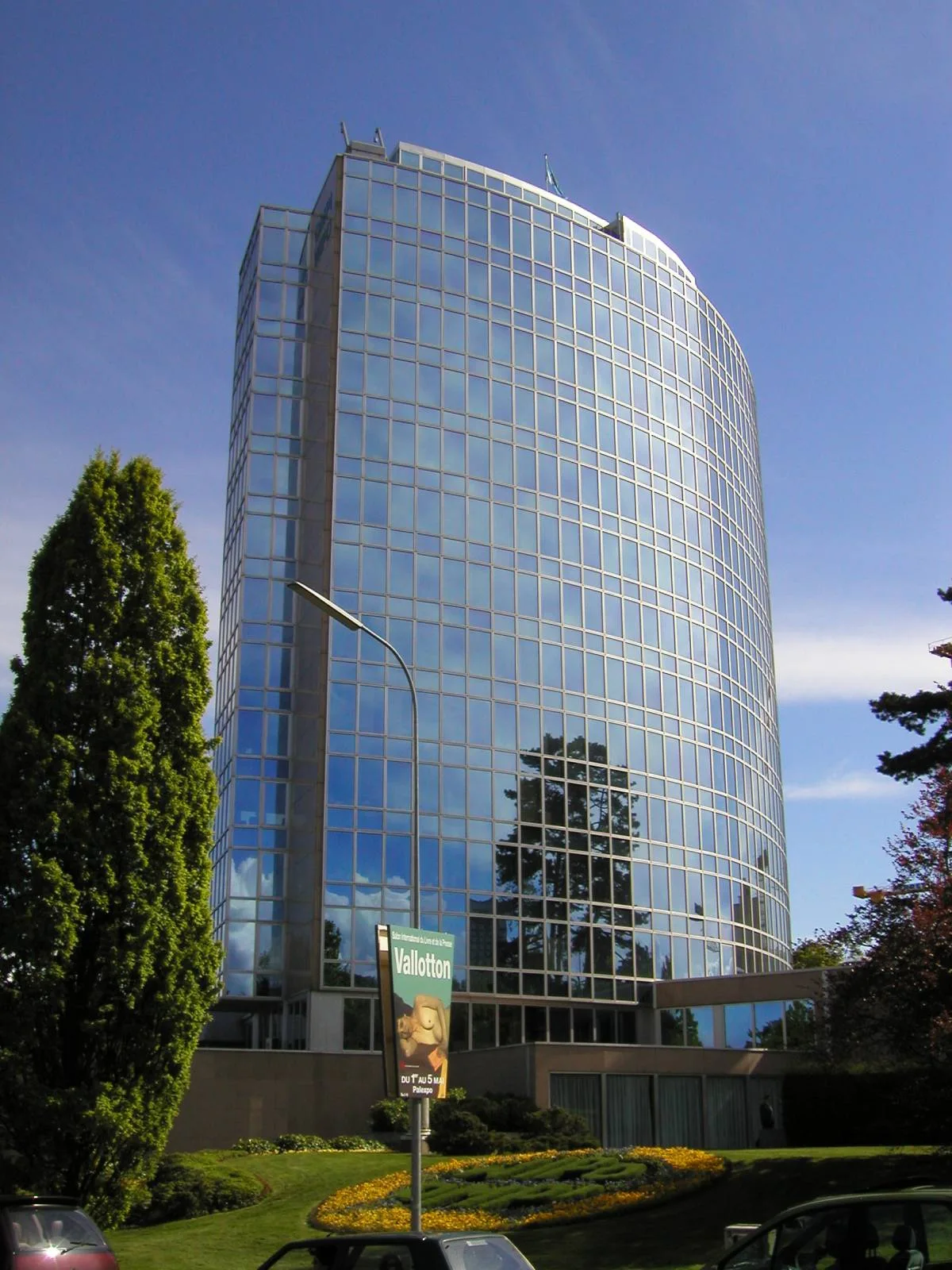 WIPO headquarters in Geneva, a curved glass tower behind trees and a flower bed