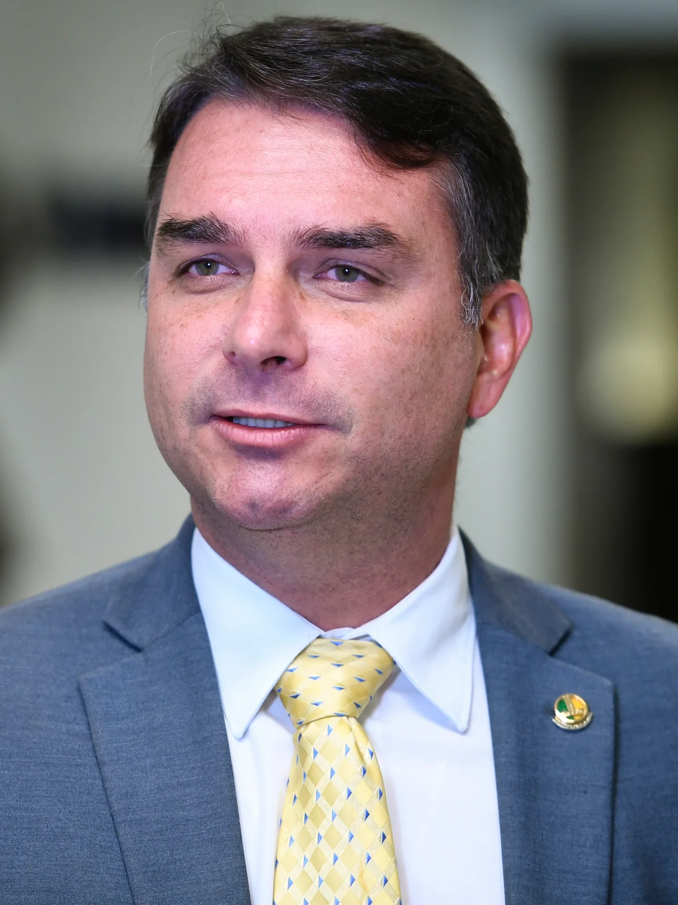 Brazilian senator Flávio Bolsonaro in a grey suit and yellow tie speaking to reporters