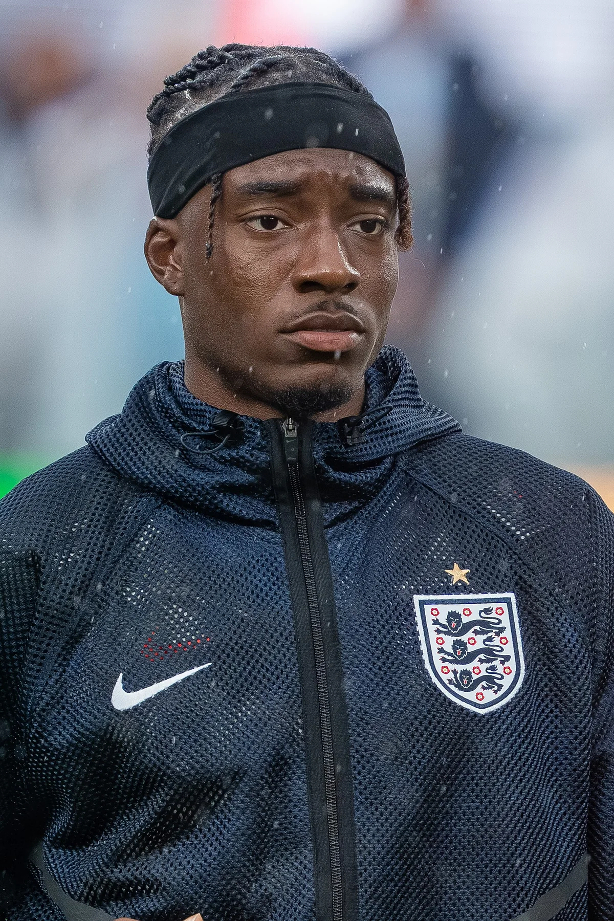 Noni Madueke in an England training jacket and headband during rain before a match
