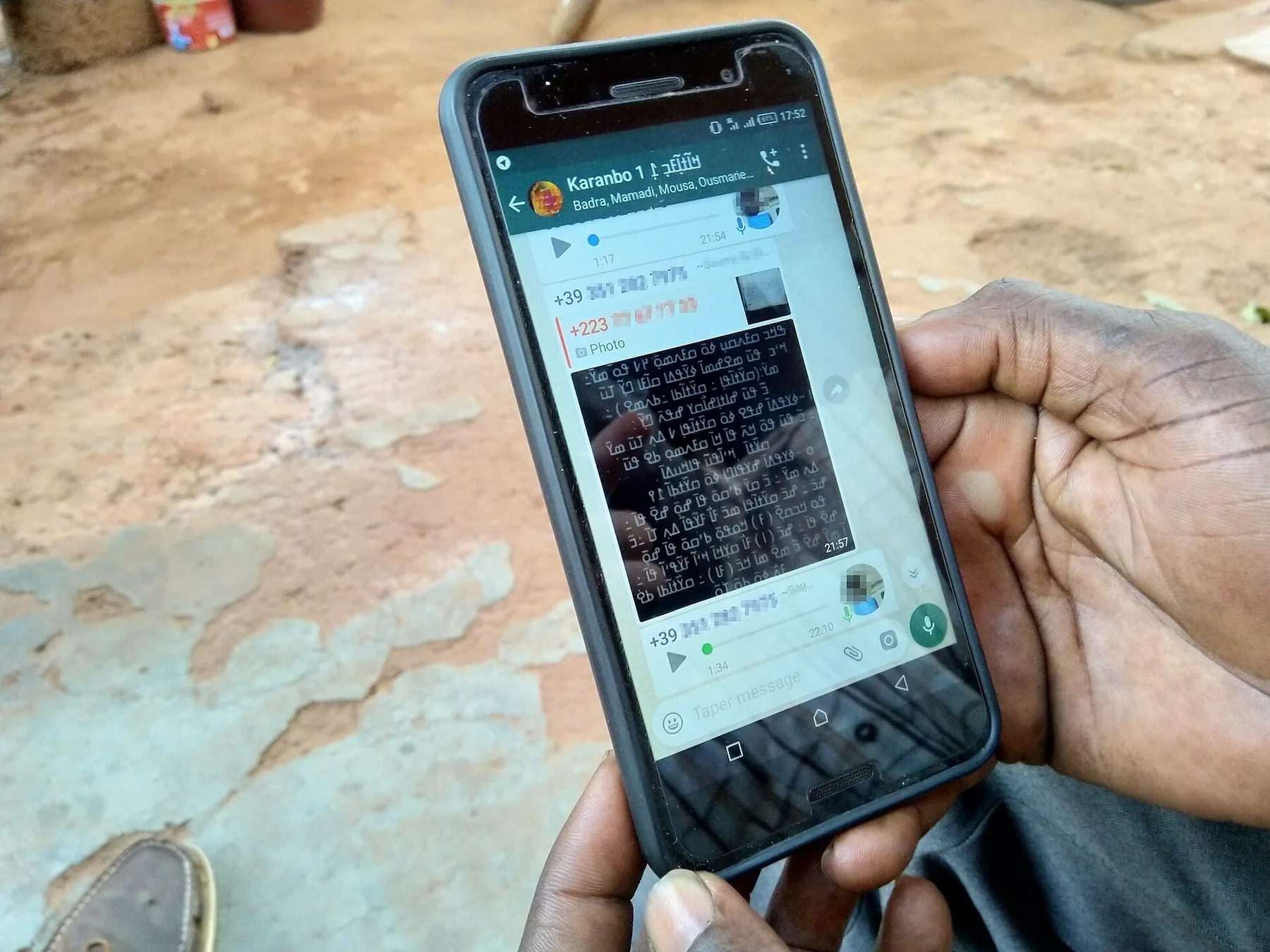 Hand holding a smartphone showing an open WhatsApp group chat with messages