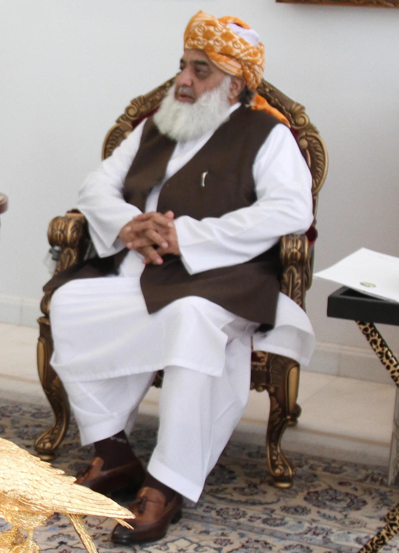Maulana Fazlur Rehman in an orange turban and brown waistcoat, seated in a carved wooden armchair