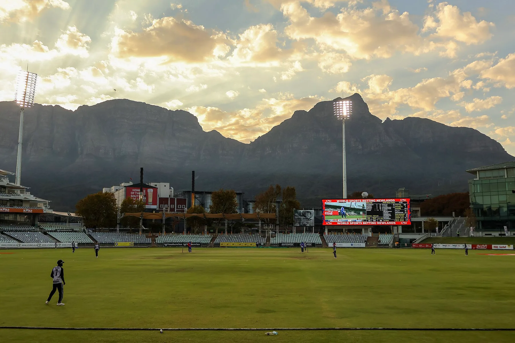 Newlands cricket ground in Cape Town with Table Mountain behind, floodlights on and fielders spread across the outfield