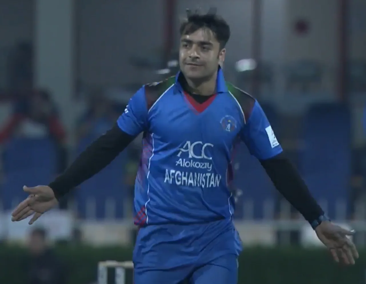 Rashid Khan in a blue Afghanistan shirt celebrating a wicket with arms spread out