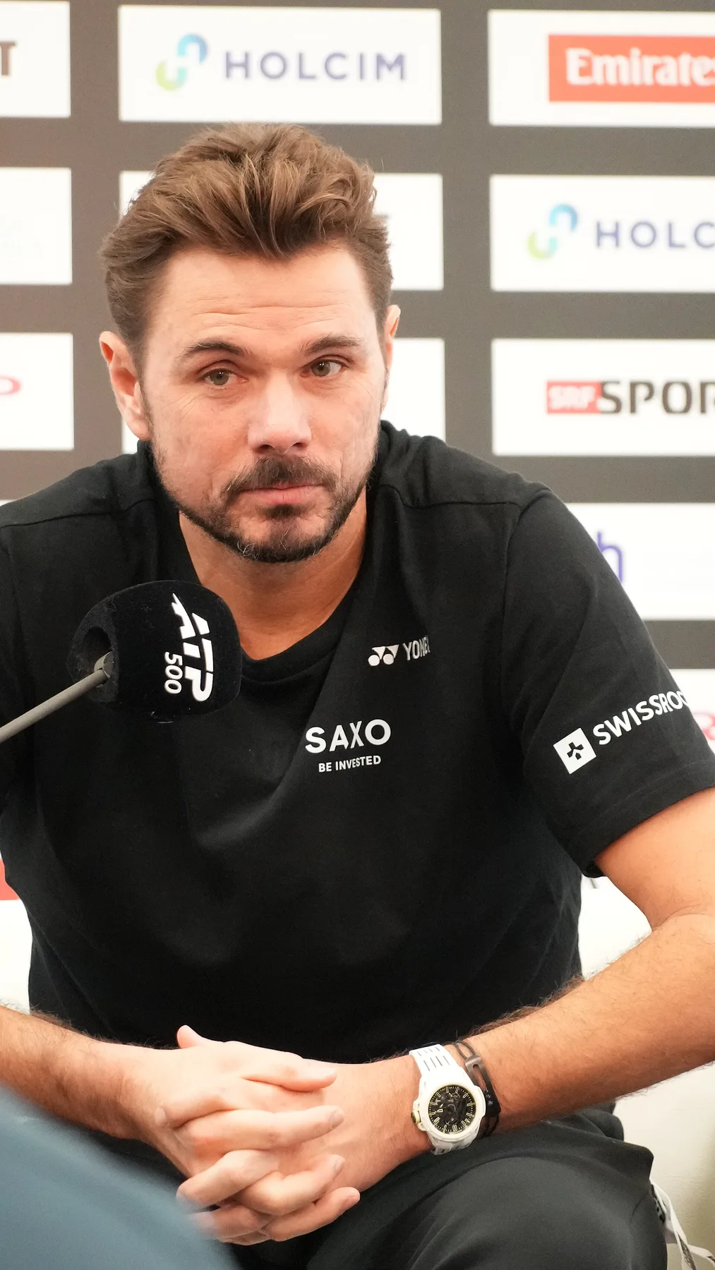 Stan Wawrinka in a black shirt speaking at an ATP 500 press conference microphone