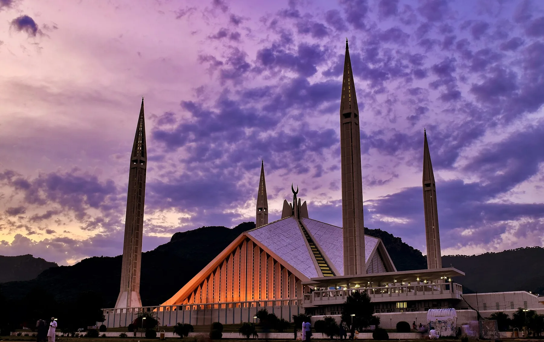 Faisal Mosque in Islamabad lit up at dusk under a purple sky with the Margalla Hills behind