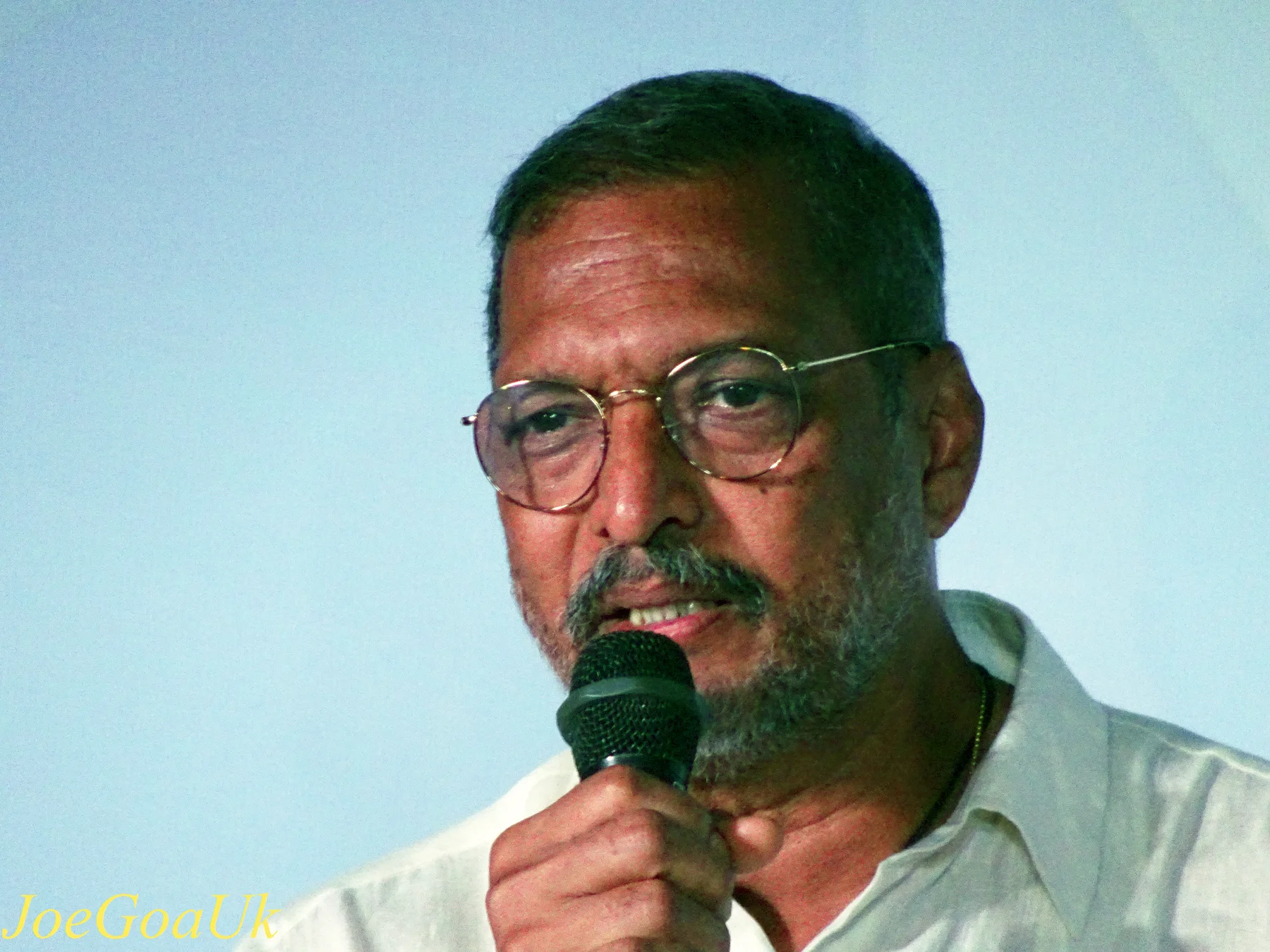 Nana Patekar in glasses and a white shirt speaking into a microphone at an event