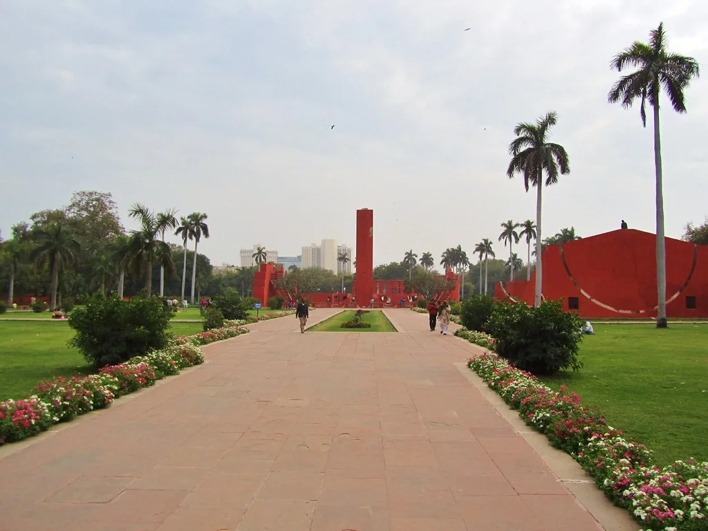 Red sandstone instruments of the Jantar Mantar observatory in New Delhi beyond a paved path, lawns and flower beds
