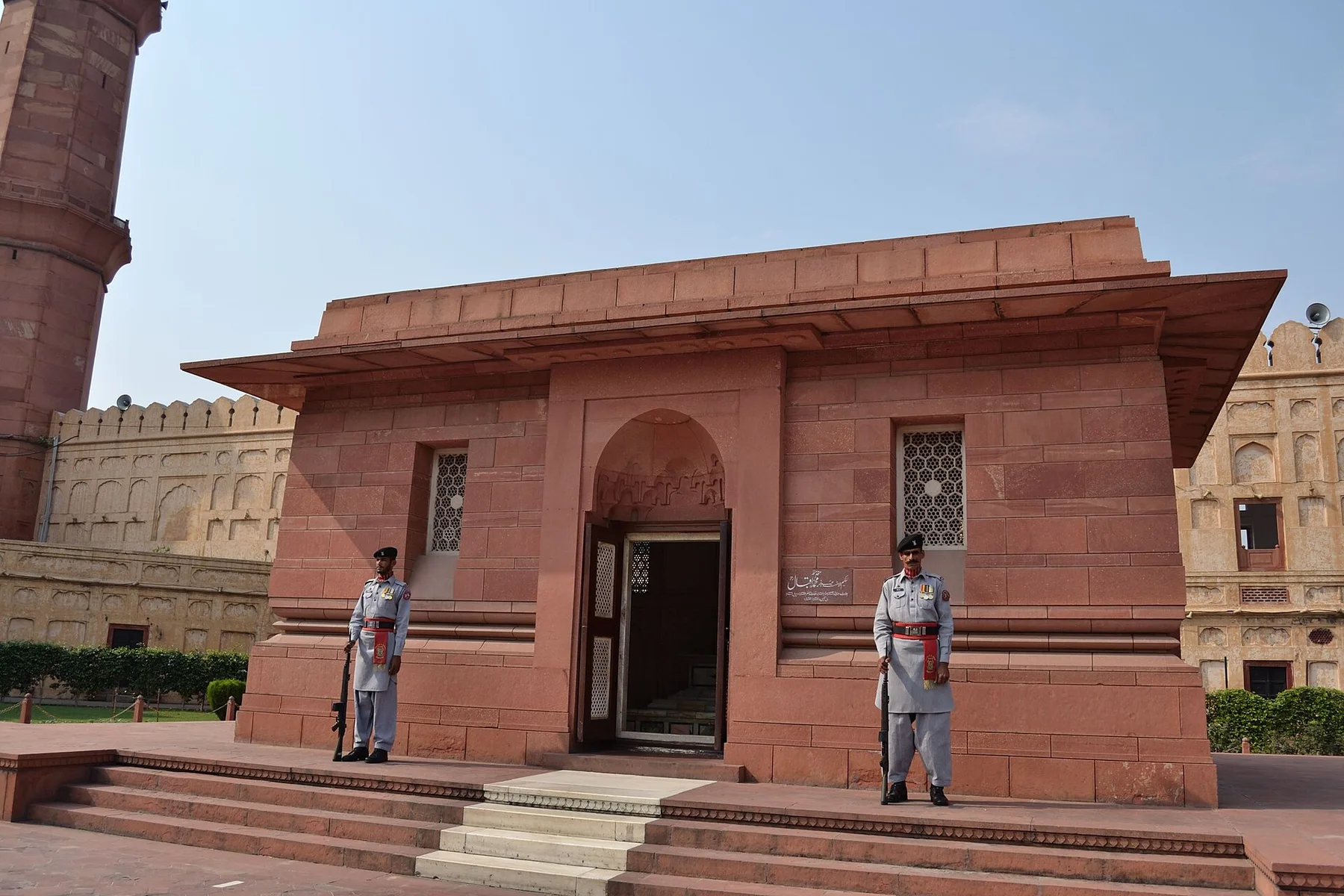 Two uniformed guards with rifles stand at the red sandstone Tomb of Allama Iqbal in Lahore
