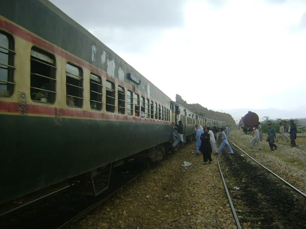 Green Pakistan Railways passenger train halted on the track as passengers stand beside the coaches
