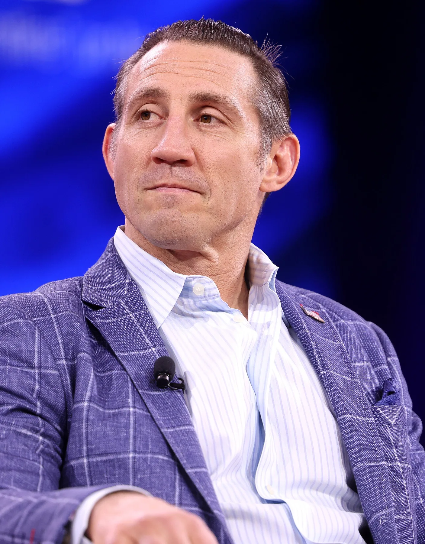 Tim Kennedy in a blue checked blazer and striped shirt seated on stage at a conference