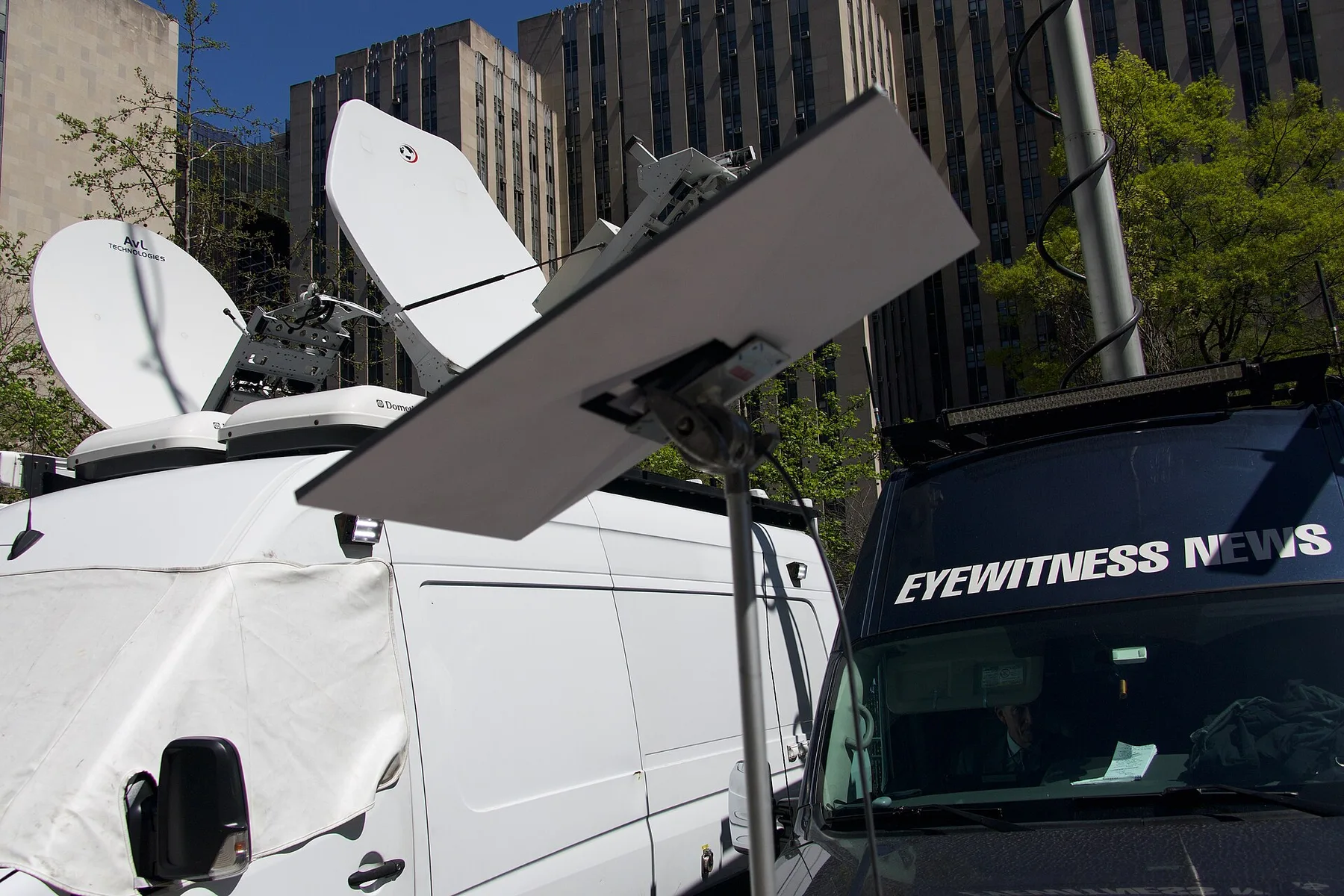 A flat rectangular Starlink dish on a pole beside satellite news vans in a city street