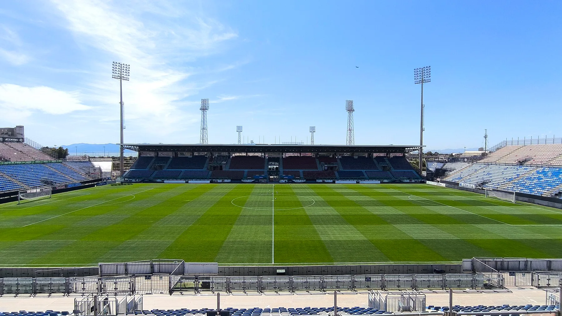 Empty Unipol Domus stadium in Cagliari with striped green pitch, floodlights and blue seats