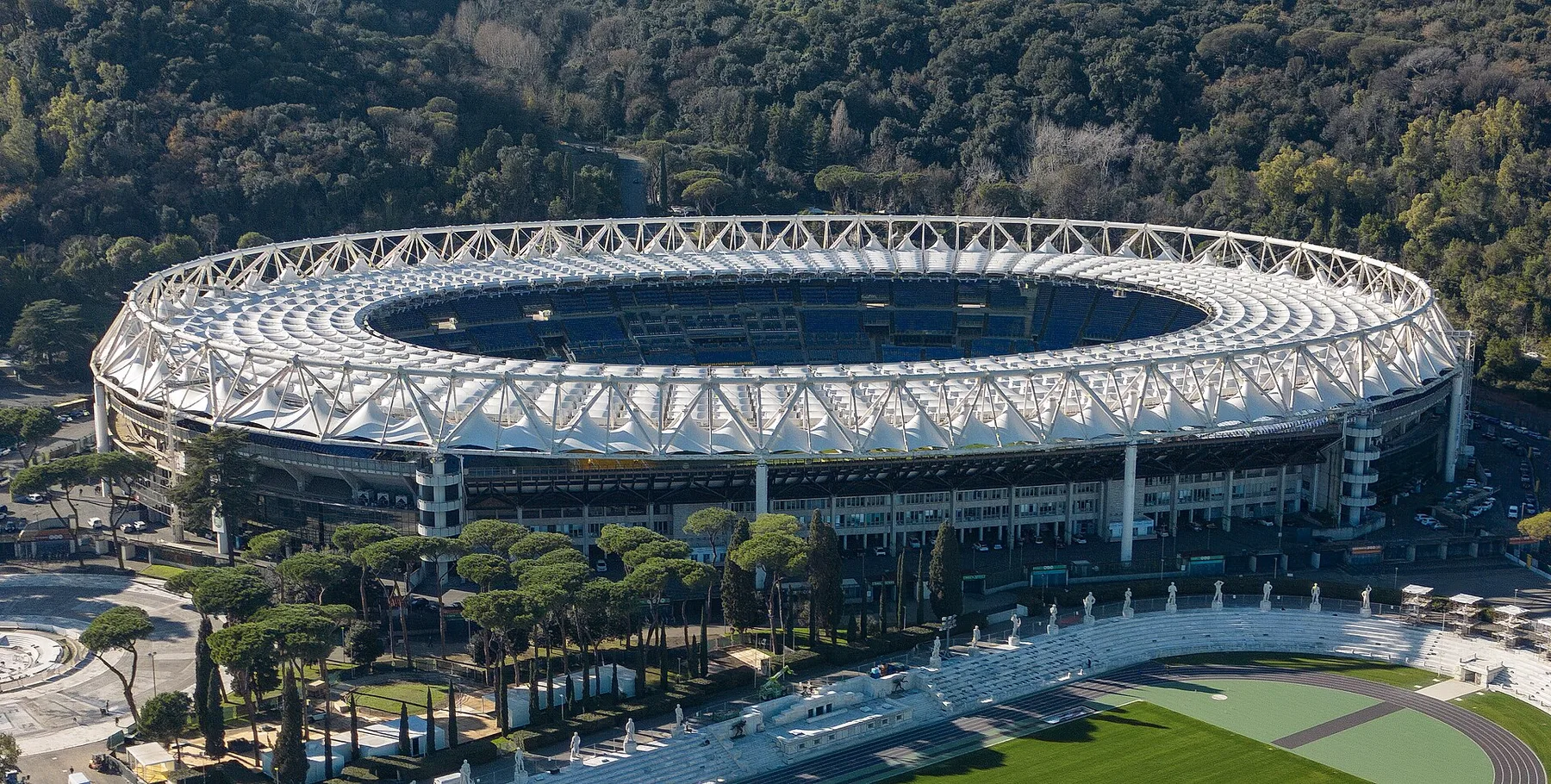 Aerial view of the Stadio Olimpico in Rome with its white roof, ringed by pine trees and wooded hills