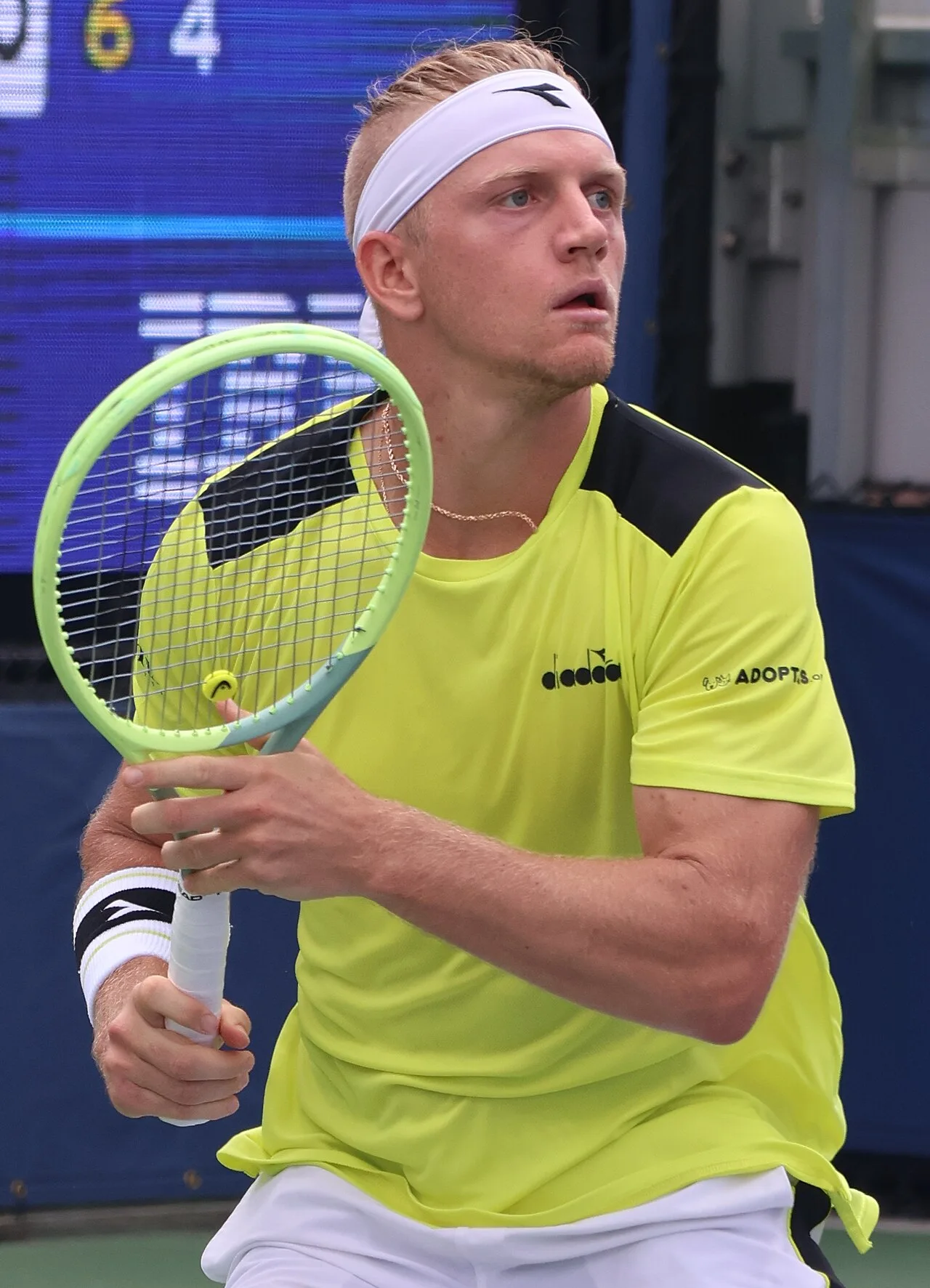 Alejandro Davidovich Fokina in a yellow shirt and white headband, racquet ready, on a hard court