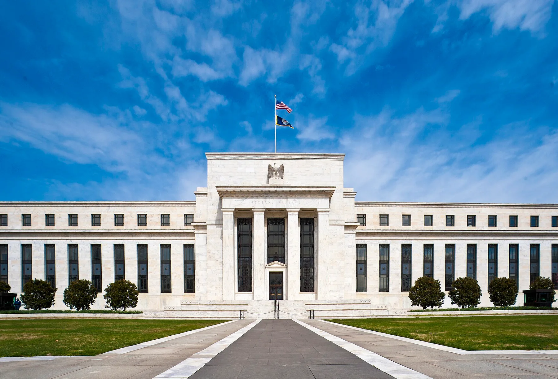 The white marble Federal Reserve building in Washington with US flags on the roof under a blue sky
