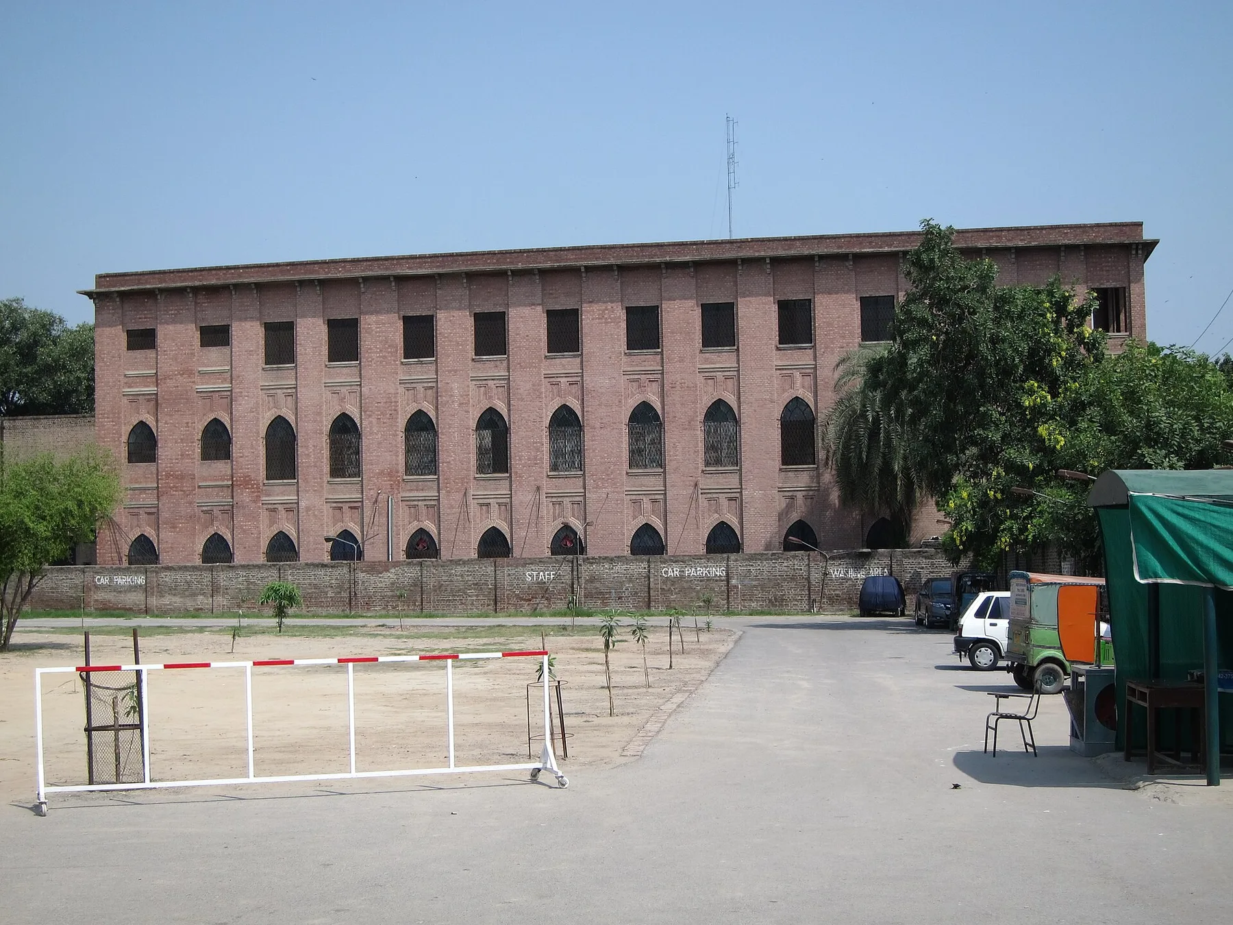 Red-brick Kinnaird College building on Jail Road, Lahore, with arched windows and a staff car park