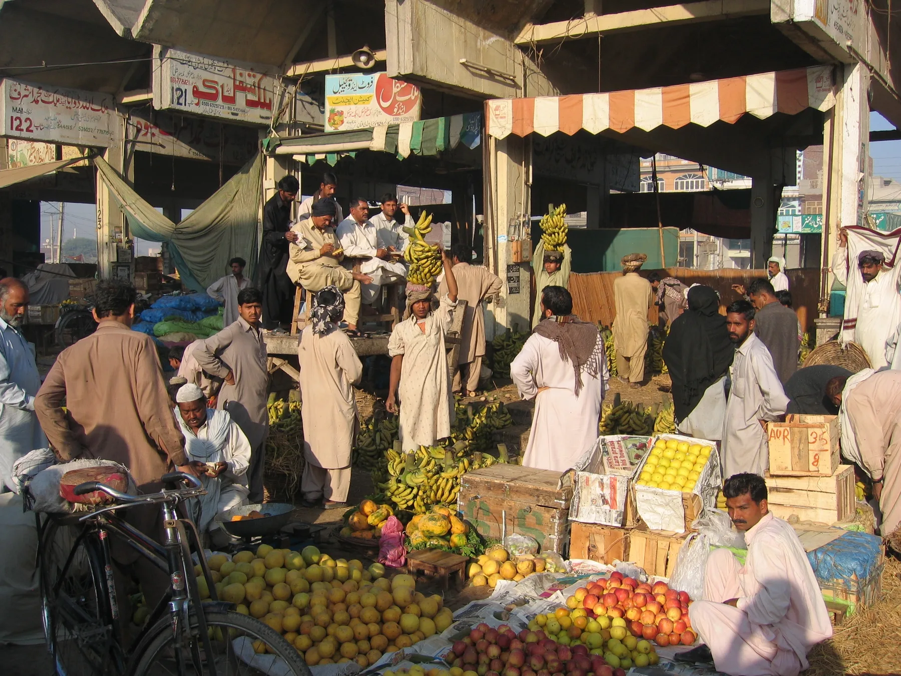Traders and buyers at a busy fruit market with bananas, apples and citrus laid out on the ground